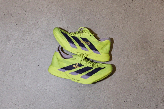 Pair of bright yellow running shoes with black stripes on a gray concrete surface