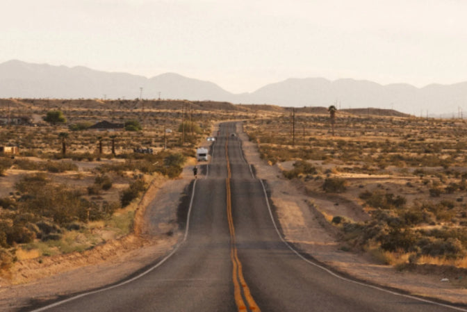 Long straight road in a desert landscape with mountains in the distance.