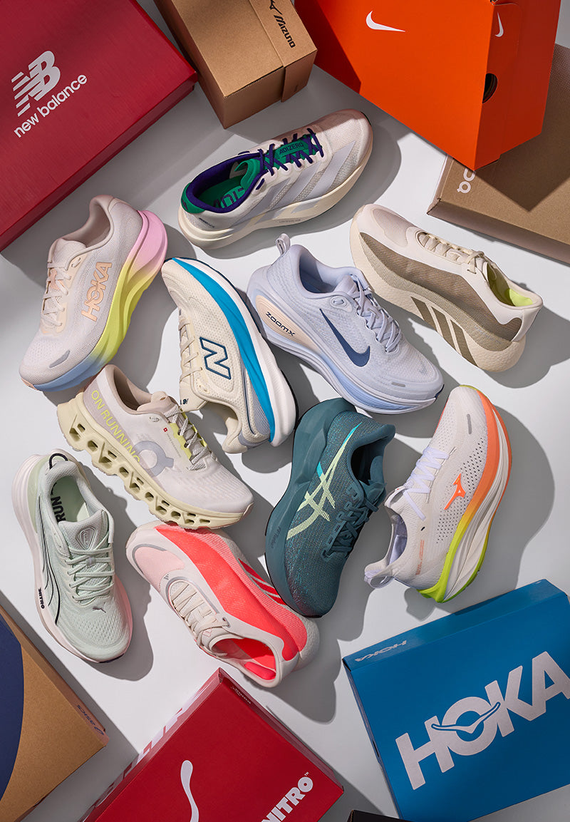 A styled flat-lay of multiple athletic sneakers in assorted colors, arranged with their branded shoeboxes on a white surface. Visible brands include New Balance, Nike, Asics, and Hoka.