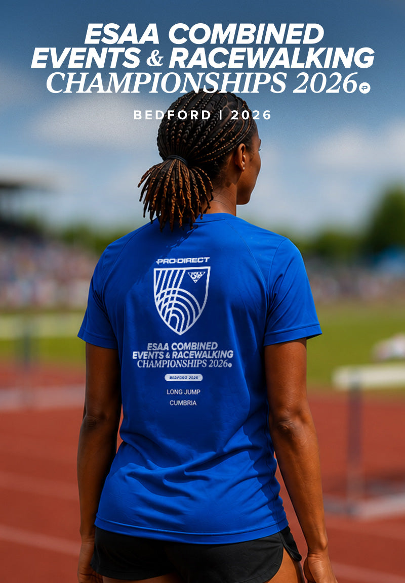 A woman standing on an outdoor track wearing a bright blue athletic T-shirt from the back, with large white event text at the top reading 'ESAA Combined Events & Racewalking Championships 2026' and 'Bedford | 2026'. The shirt has a large white printed logo and text on the back.