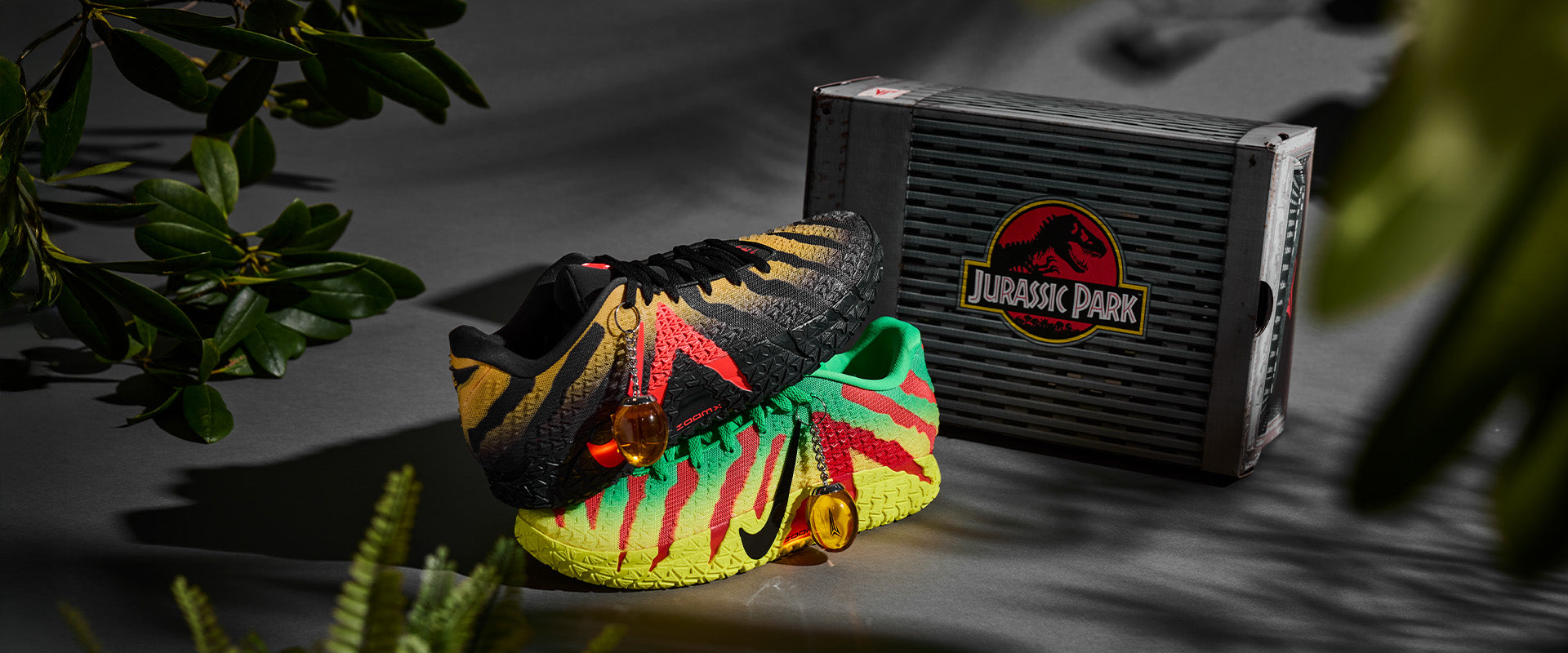 Colorful sneakers with a 'Jurassic Park' box on a dark surface with greenery.