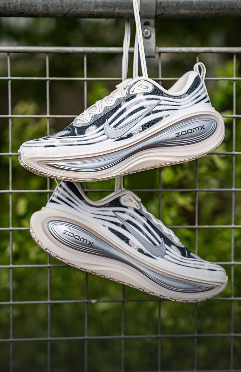 Pair of white and black running shoes with 'ZoomX' branding hanging on a metal fence.