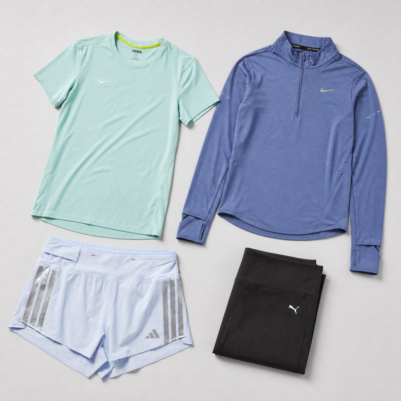 Set of athletic clothing including a green t-shirt, blue long-sleeve top, light blue shorts with Adidas logo, and black leggings on a gray background.