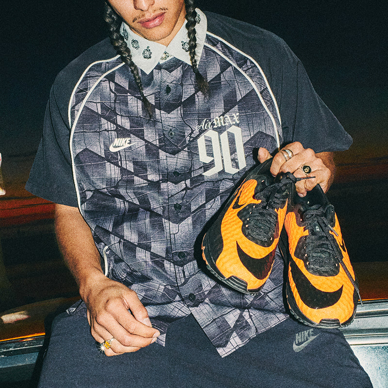 Person holding a pair of orange and black Nike trainers, wearing a patterned shirt.