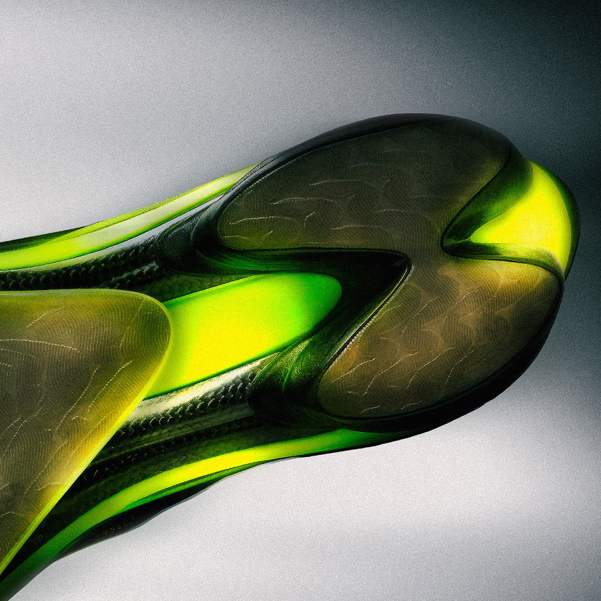 A close-up studio shot of a translucent athletic shoe sole or component with layered sculpted panels in dark olive, emerald green, and neon yellow-green on a gray gradient background.