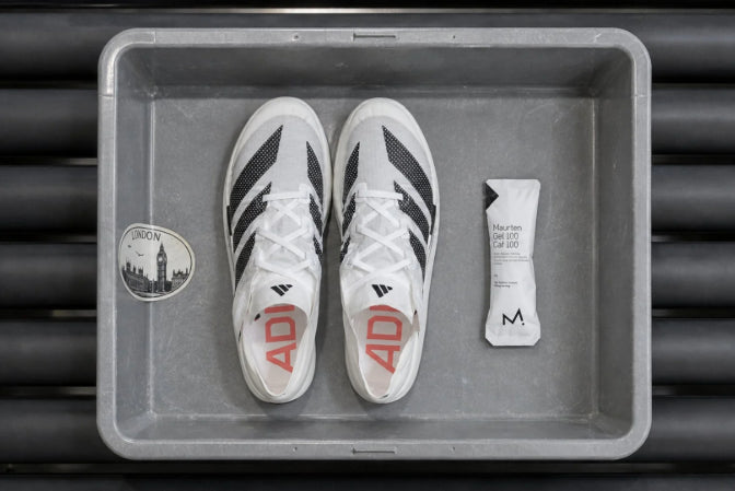 White athletic shoes with black and red accents on a gray tray, next to a small white container.